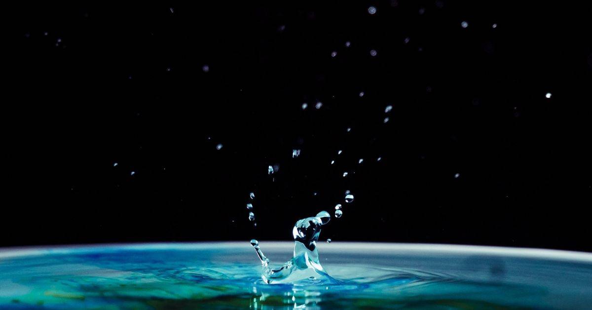 Blue-green water drop splashing against a black background